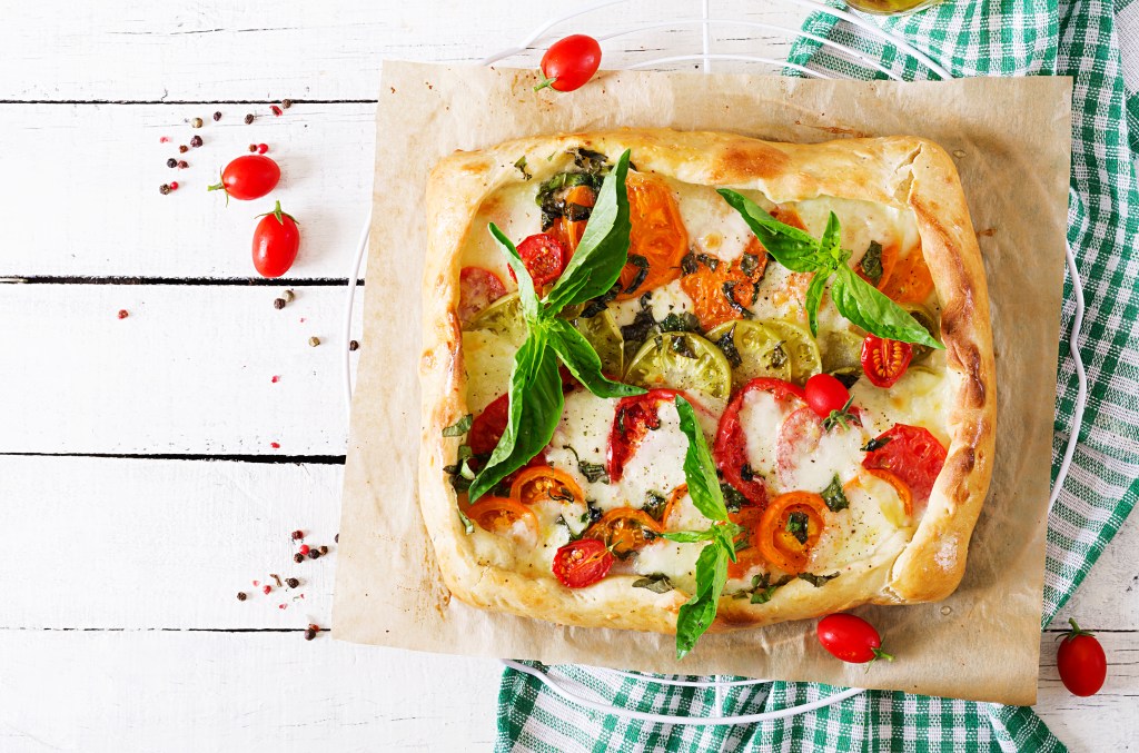 Mozzarella, tomatoes, basil savory pie on a white wooden background. Delicious food, appetizer in a mediterranean style. Top view. Flat lay